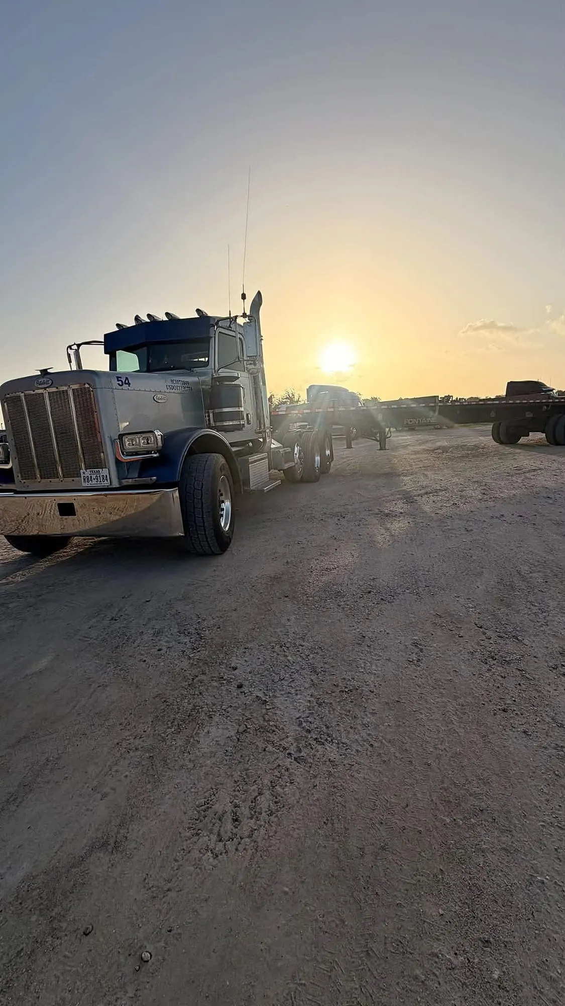 MDJ Peterbilt 389 day cab, truck 54, parked at the Port Arthur yard at sunset with flatbed trailers staged behind it.