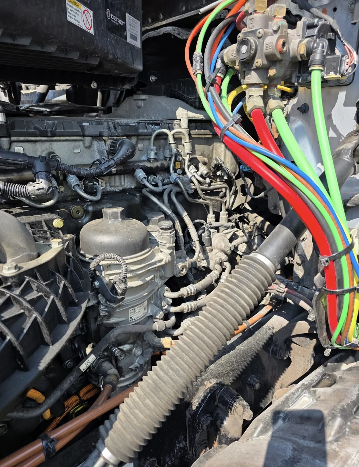 Under the hood of a Detroit-powered truck: air conditioning compressor, power steering lines, and color-coded air lines routed along the frame rail.